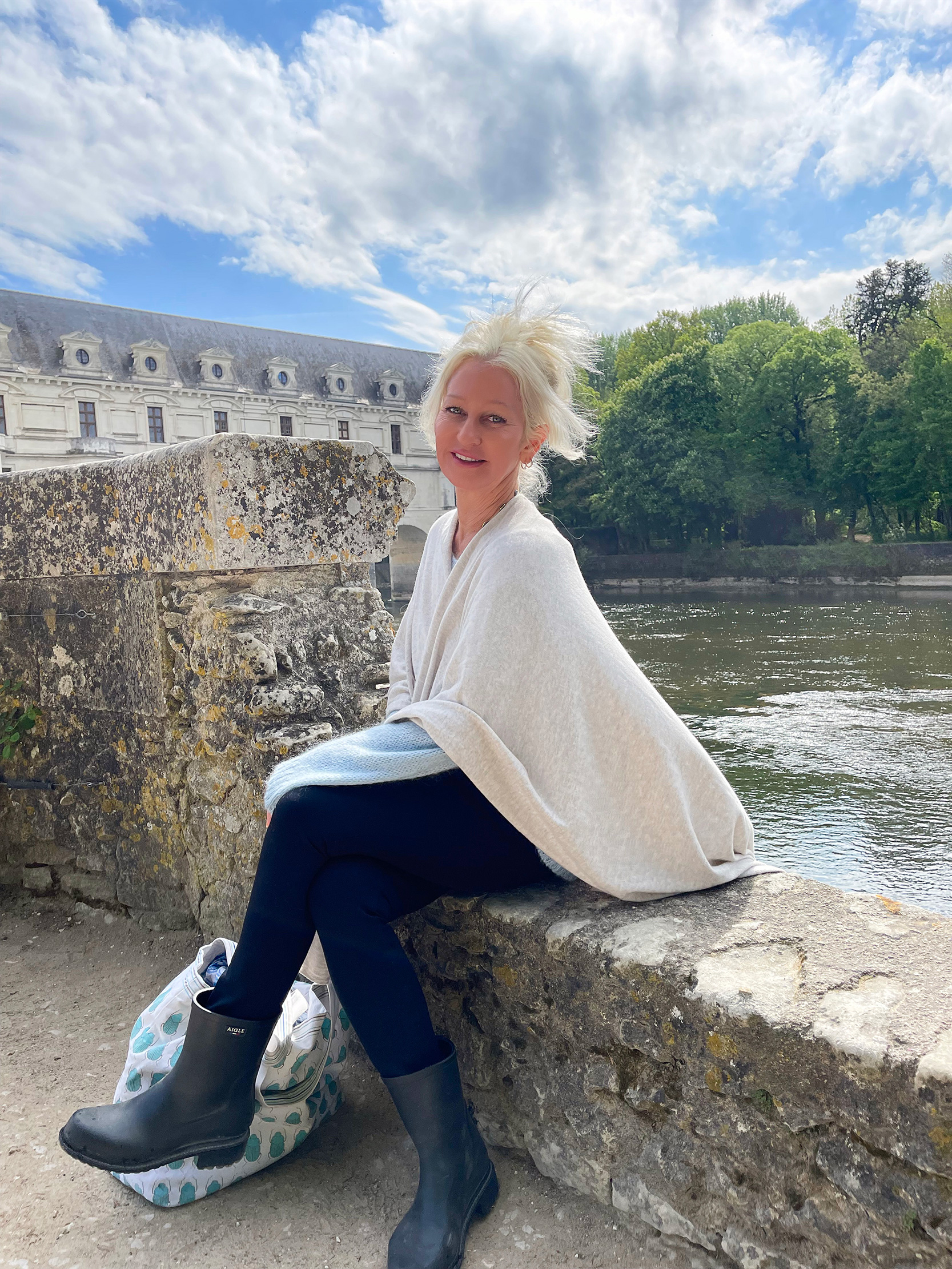 Christy Destremau, founder of France Off the Beaten Path™, sitting in front of the beautiful lake, and old castle