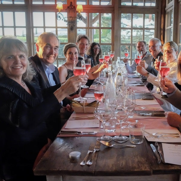 A group of happy people are toasting with raised glasses. Check our Bordeaux Tour Itinerary